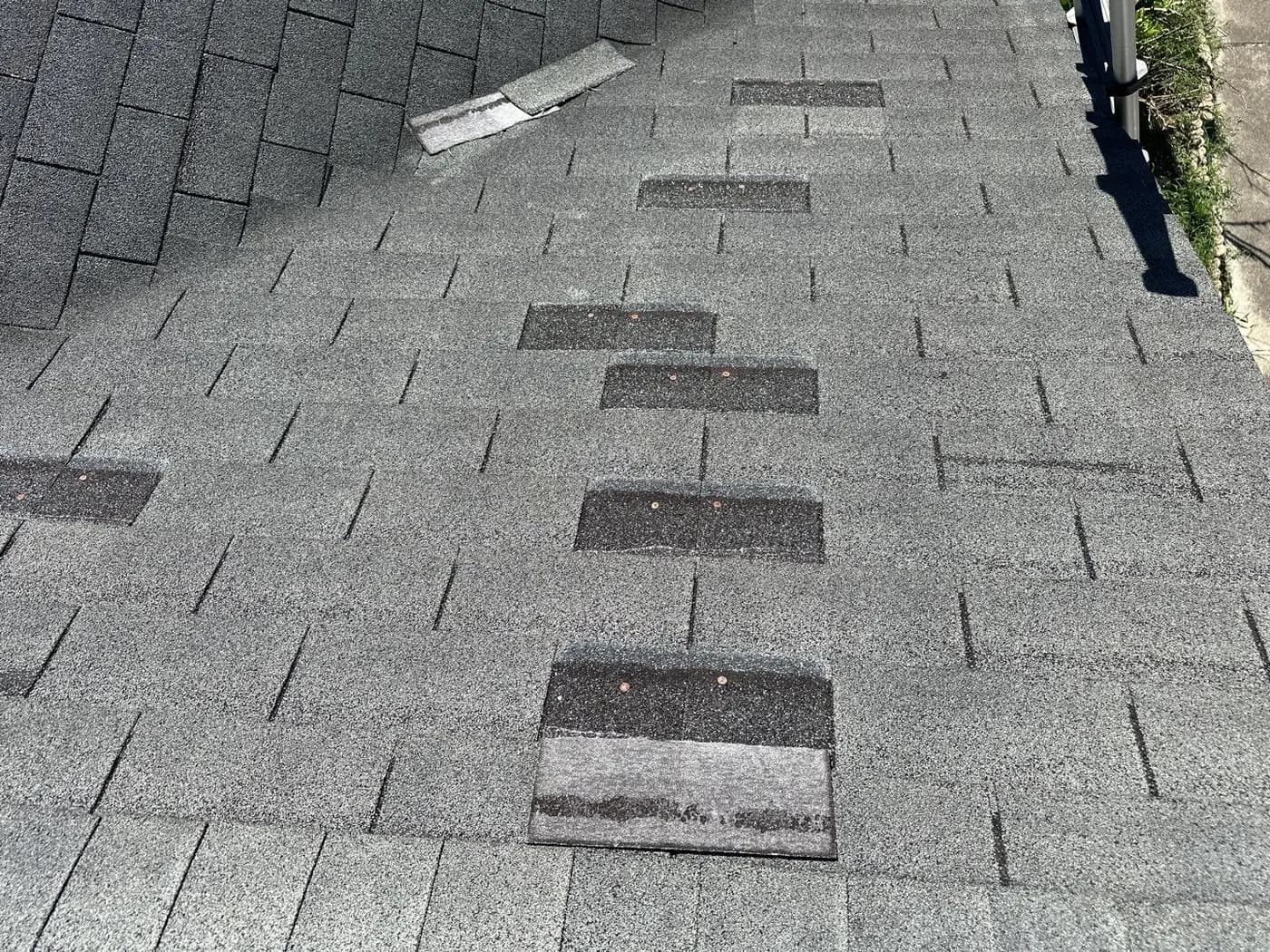 Existing roof shingles with several visible prior repair areas documented before tear-off.